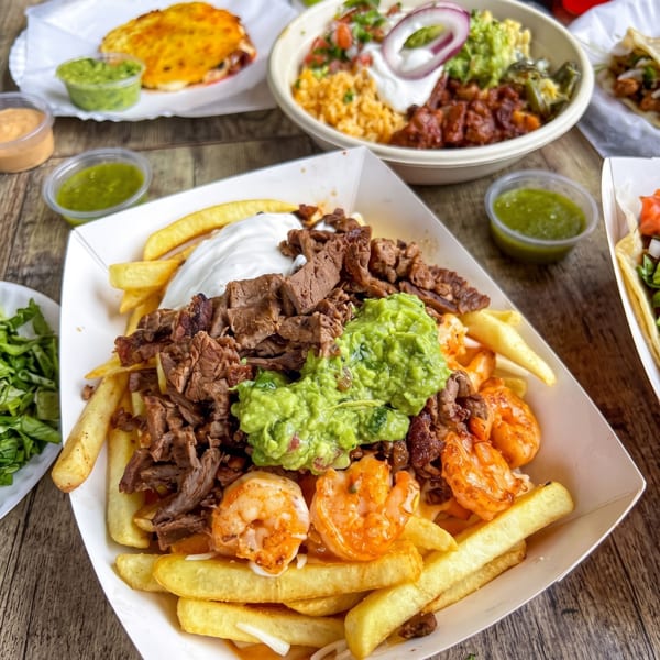 Loaded fries with steak, shrimp, guacamole, and sour cream, surrounded by other Mexican dishes.