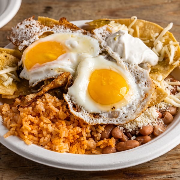 A plate of chilaquiles with two fried eggs, rice, beans, sour cream, and cheese.