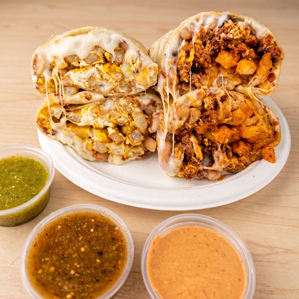 Two cheesy burritos, cut in half, revealing fillings, served with three dipping sauces.