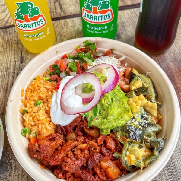 A colorful Mexican food bowl with rice, meat, guacamole, salsa, and sour cream, with three Jarritos sodas.